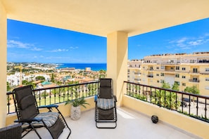 Een balkon met twee loungestoelen, een bloempot en uitzicht op een kustplaats en de zee.