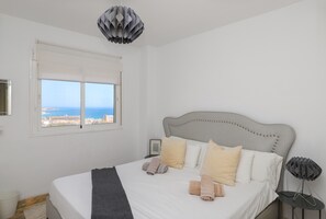 Ein Schlafzimmer mit einem Bett, Kissen, einem Nachttisch, einer Lampe und einem Fenster mit Blick.