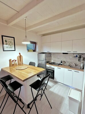 A modern kitchen with white cabinets, a wooden island with chairs, a hanging light, and a framed botanical print on the wall. - Mreznica - Zelena oaza I (Generalski Stol)
