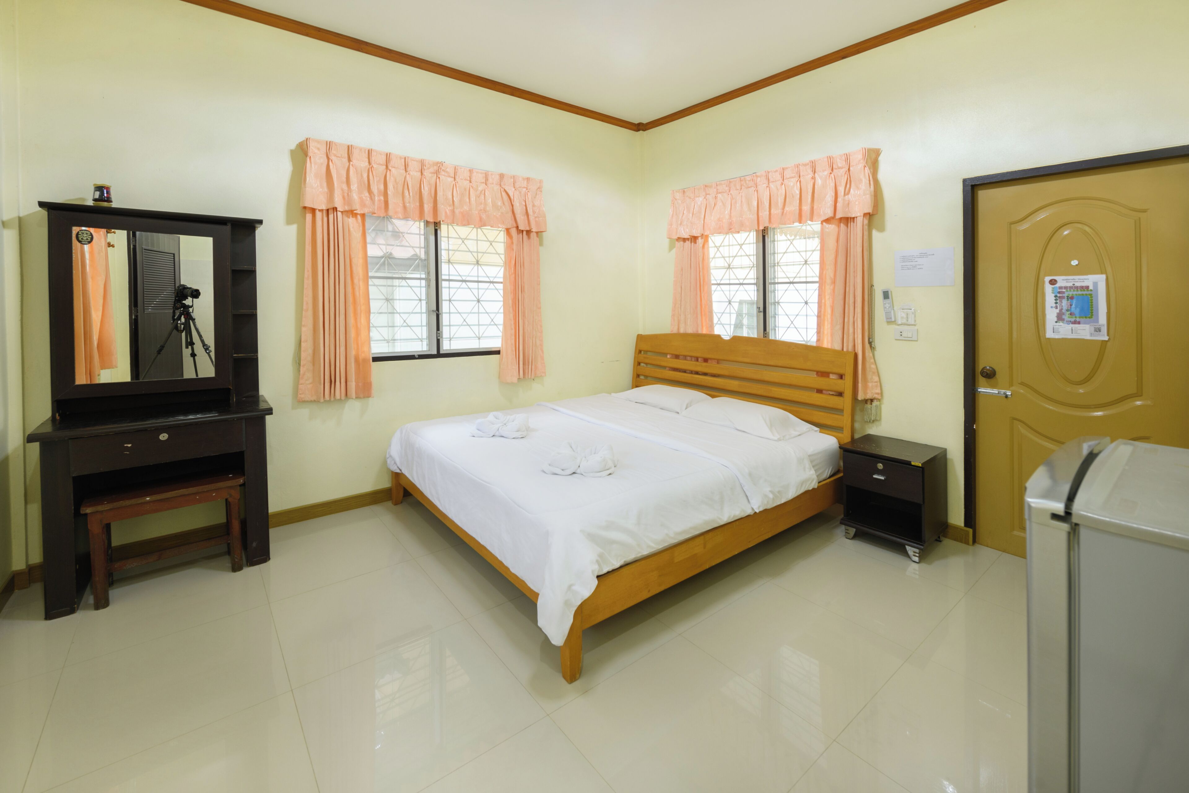 A bedroom with a bed, a dresser, a mirror, a desk, a window with curtains, and a door.
