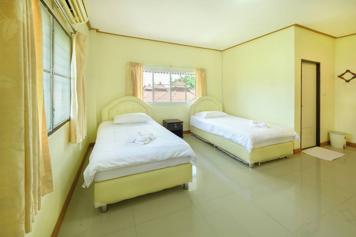A hotel room with two beds, a window with curtains, a door, and a tiled floor.