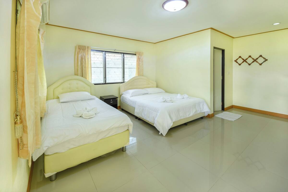 A hotel room with two beds, a window with curtains, a flat-screen TV, and a door.