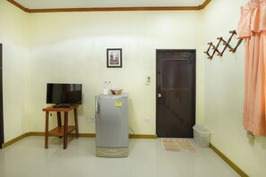 Una habitación con televisión de pantalla plana, refrigerador, taburete de madera, una puerta y perchero en la pared.