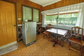 Una cocina con refrigerador, una mesa de comedor, sillas y un ventanal con cortinas.