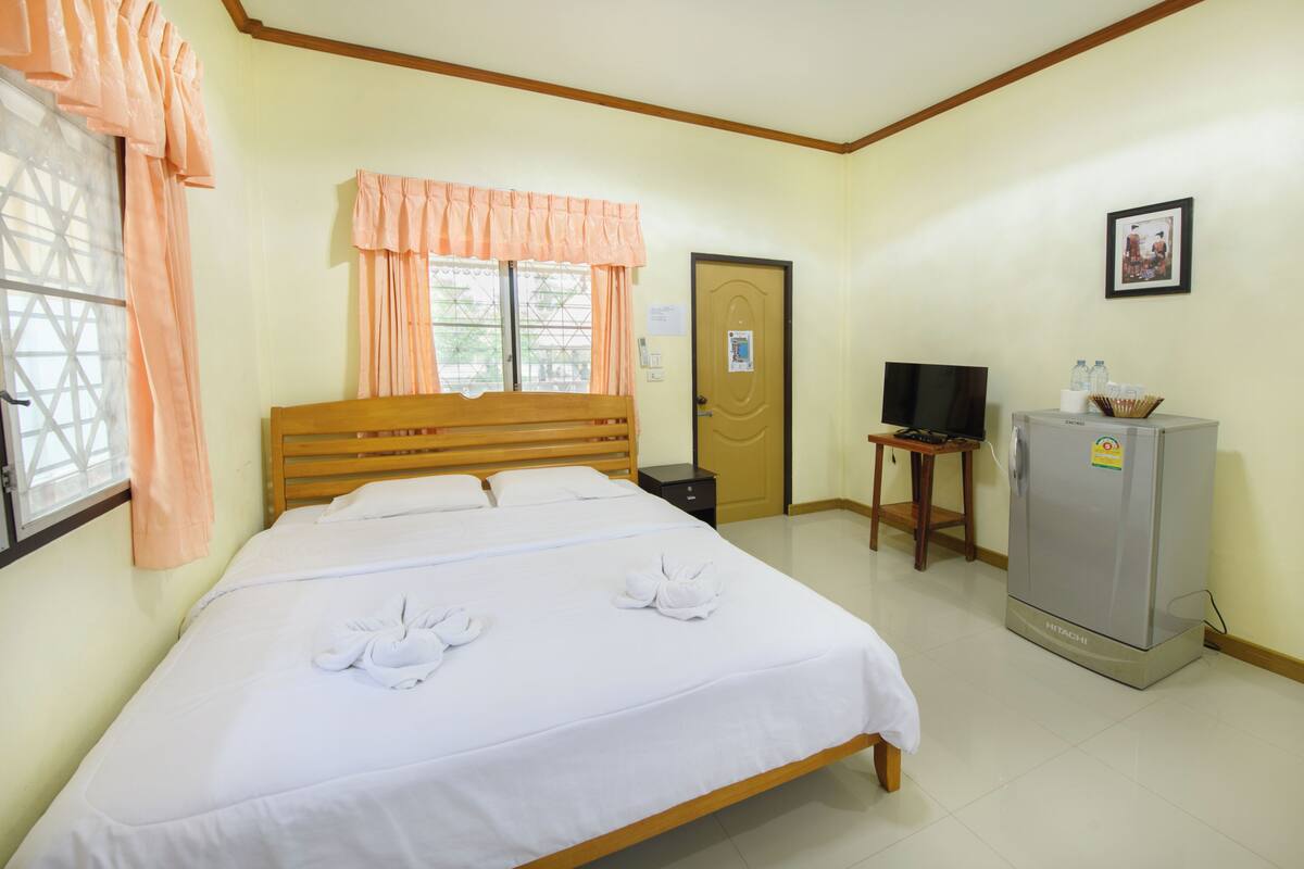 A hotel room with a bed, a television, a refrigerator, and a window with curtains.