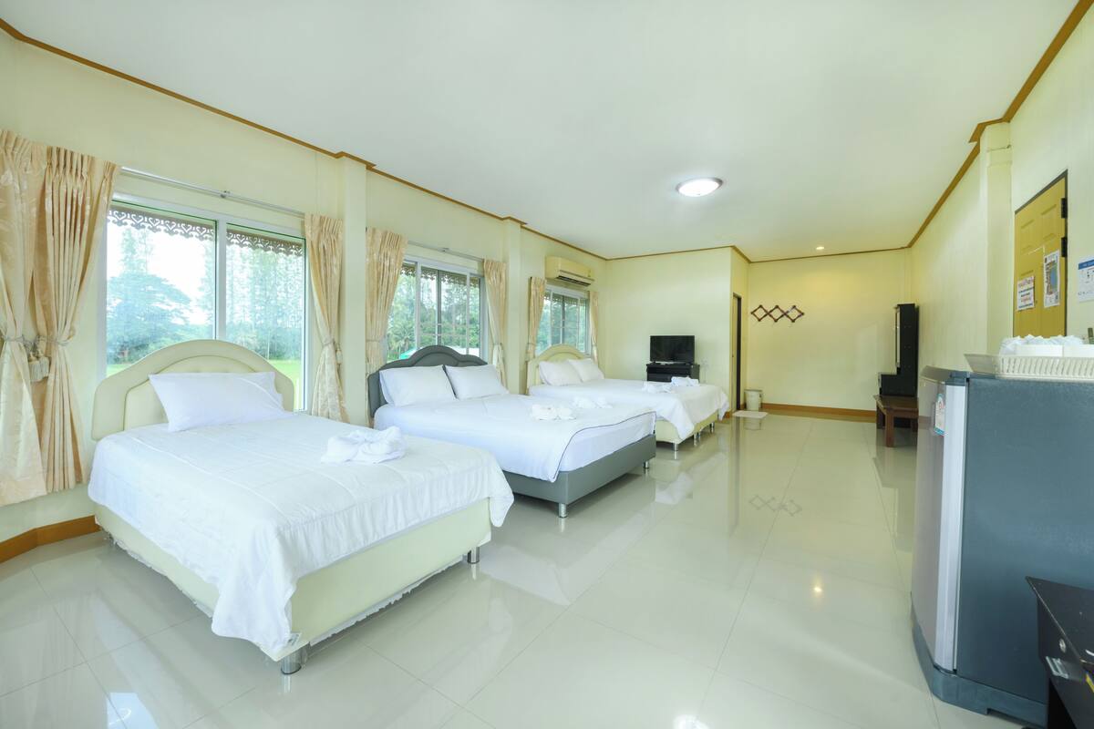 A hotel room with three beds, a television, and a refrigerator.