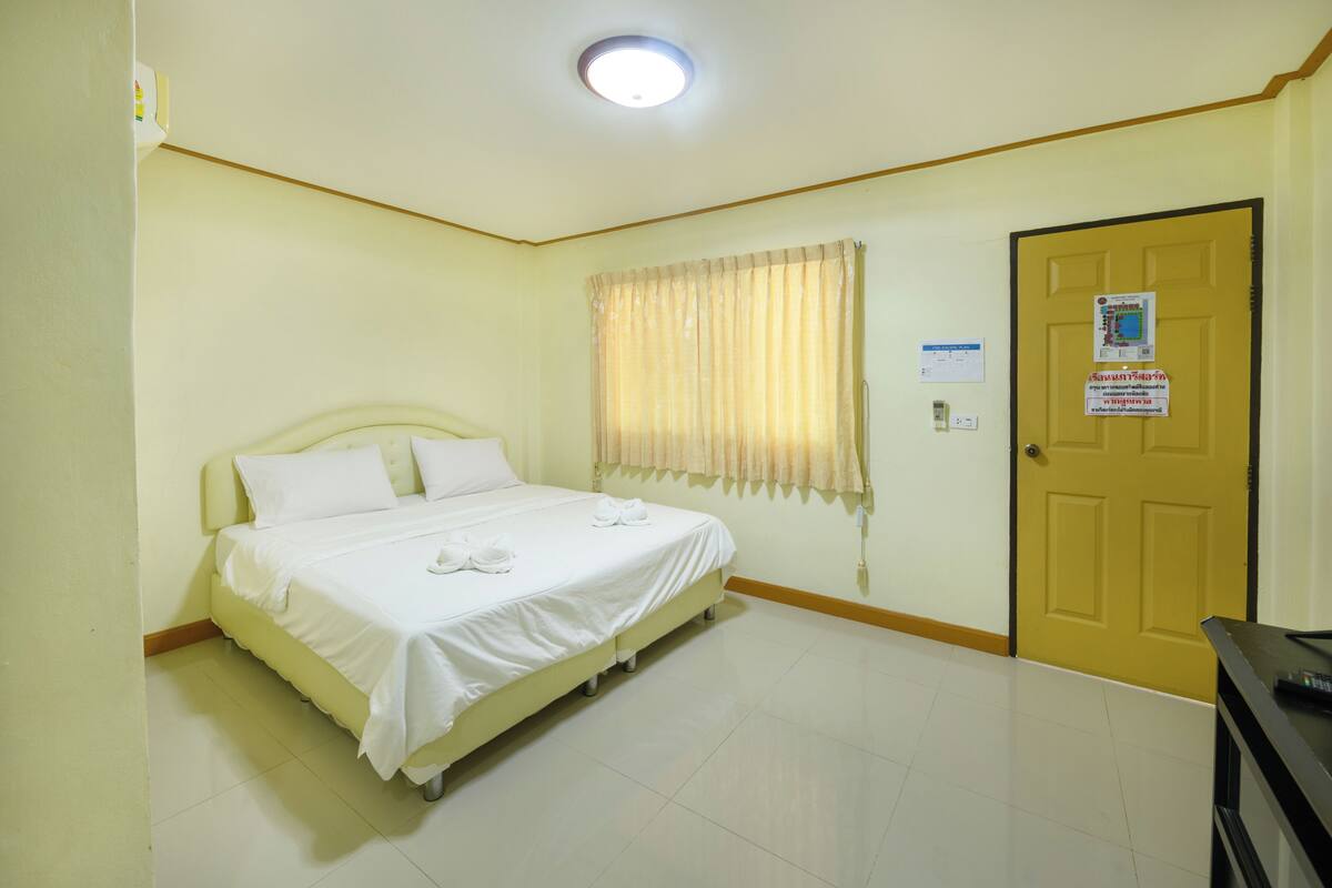 A hotel room with a bed, a door, a window with curtains, and a light fixture.