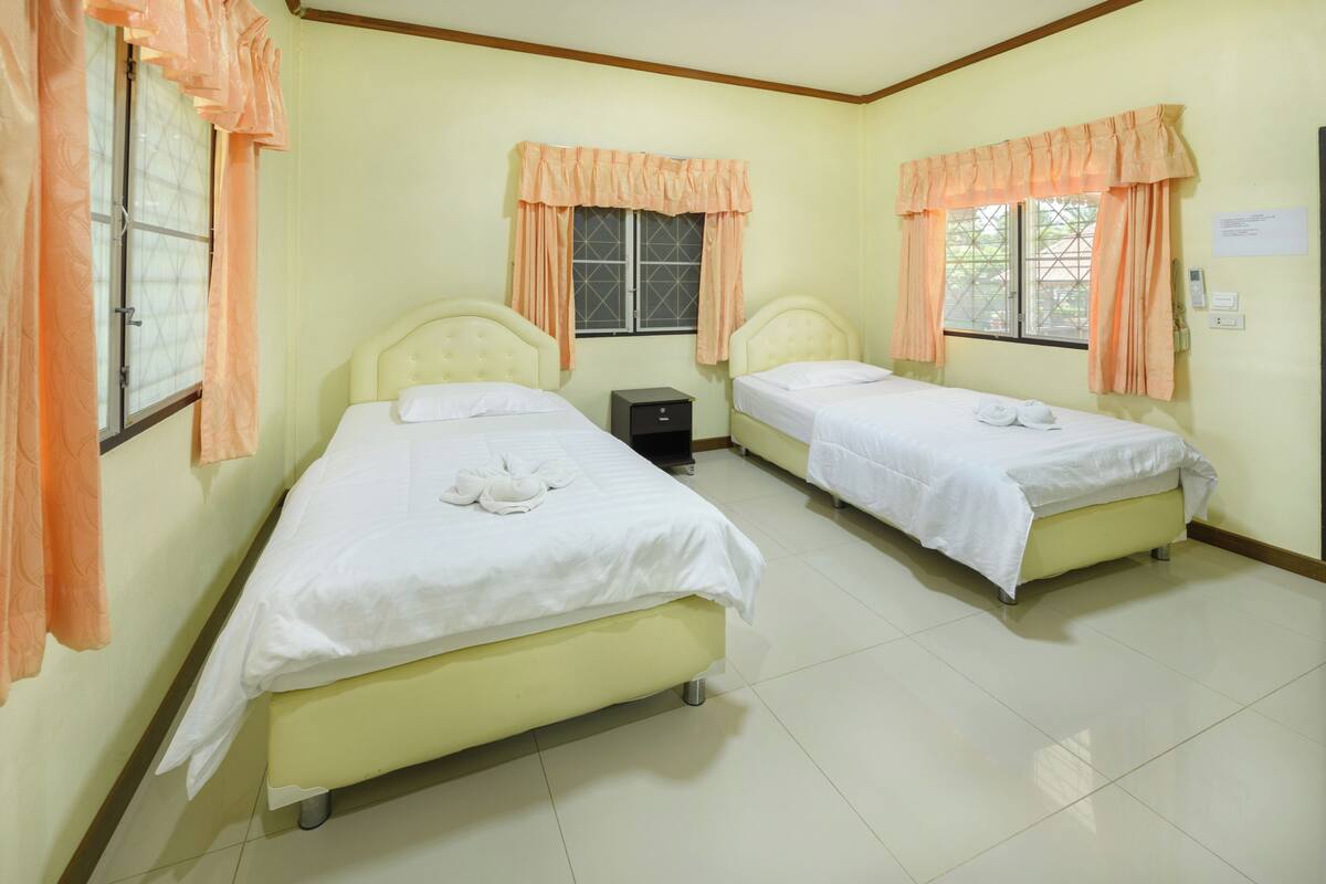 A room with two beds, a nightstand, and a window with curtains.