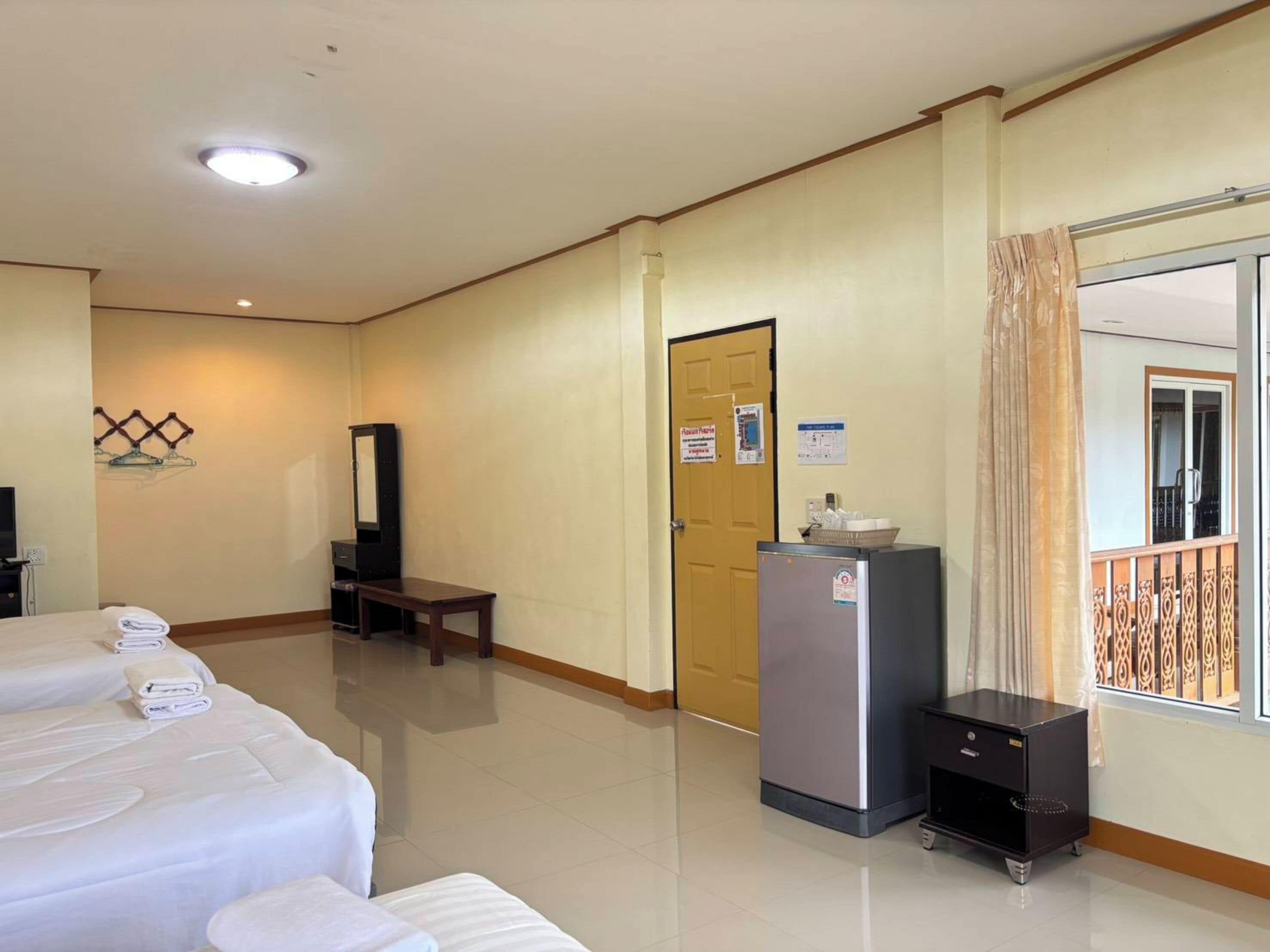 A hotel room with two beds, a desk, a refrigerator, and a window with a balcony.