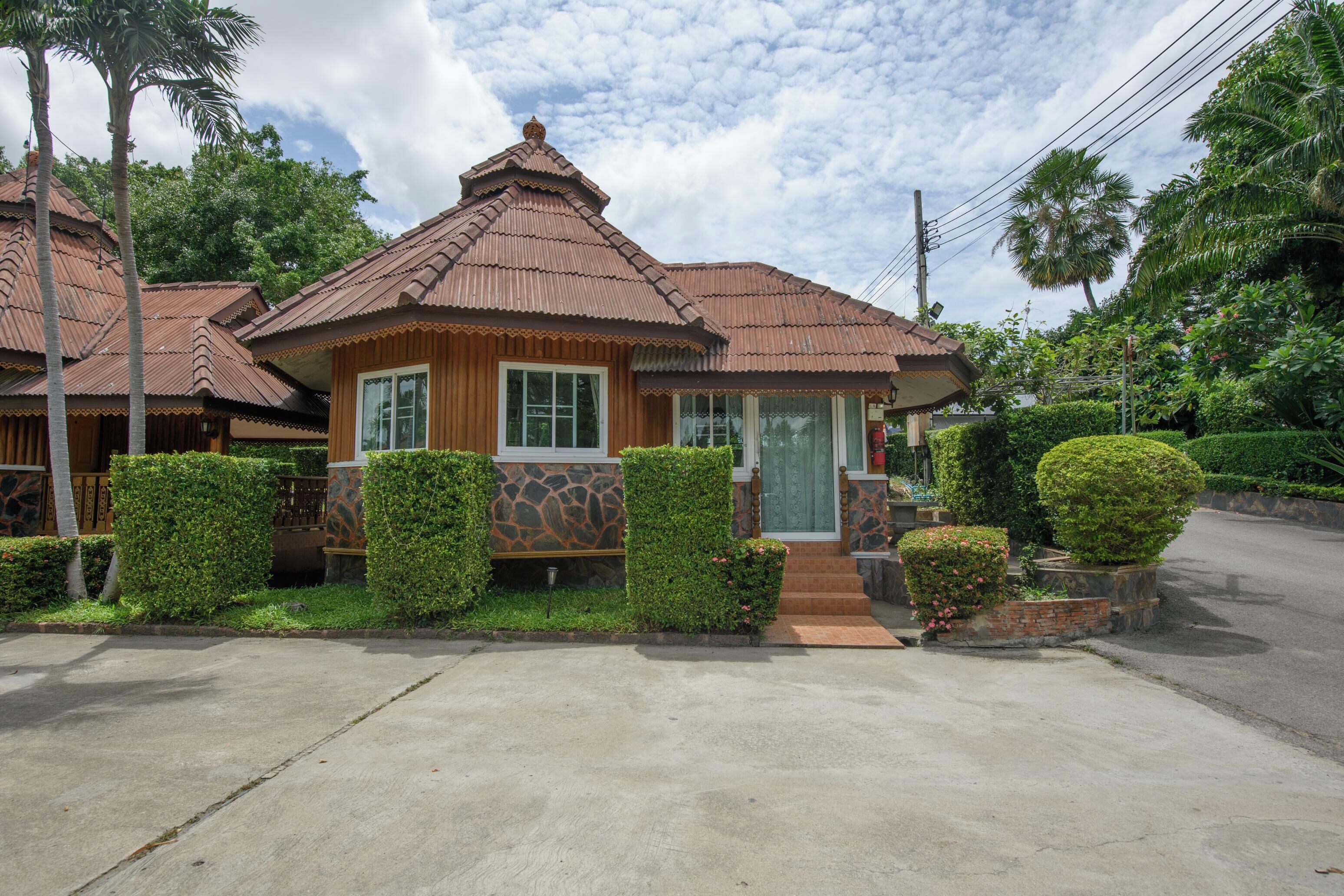 Una casa de madera tradicional con techo de tejas, rodeada de setos cuidados y una palmera.
