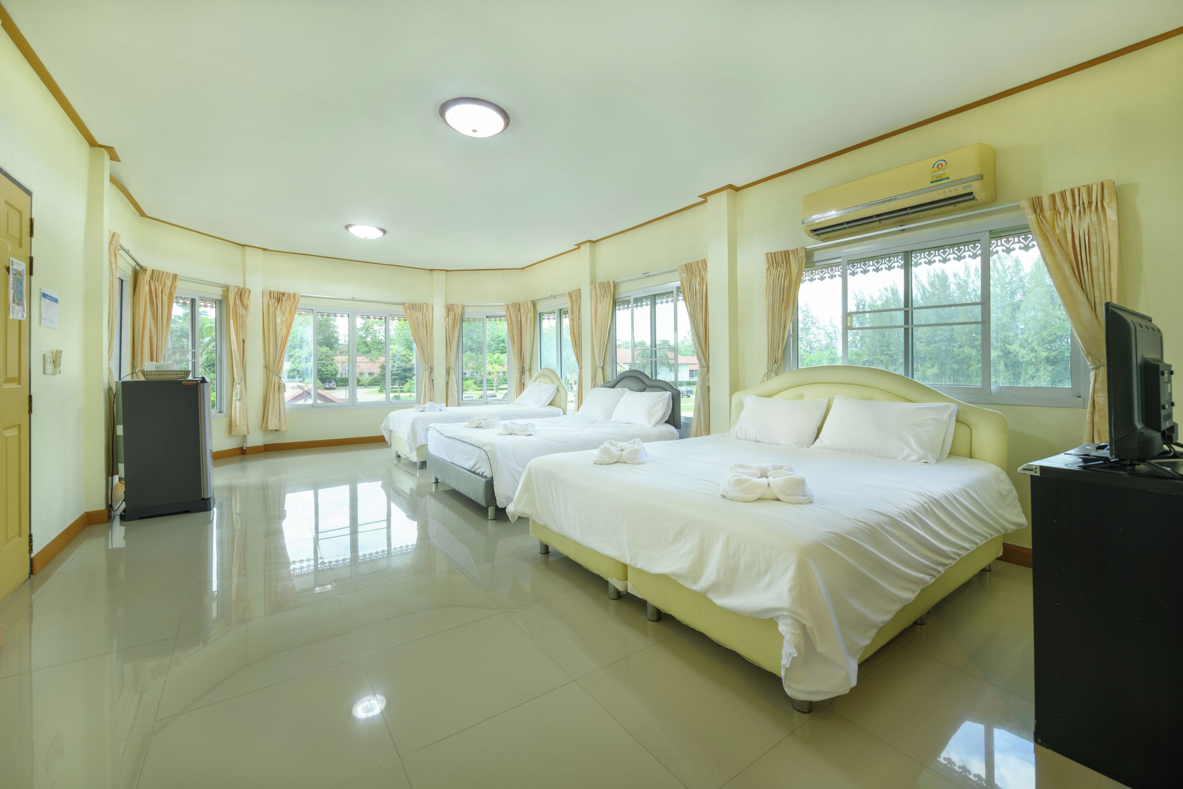 A hotel room with three beds, a flat-screen TV, and an air conditioning unit.