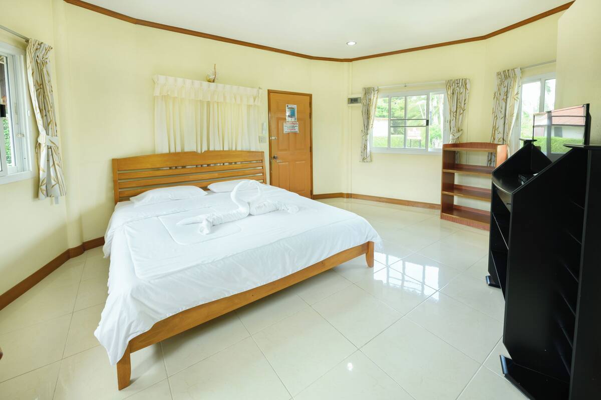 A bedroom with a wooden bed, a door, windows, and a black TV stand.