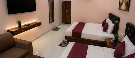 A hotel room with two beds, a sofa, a TV, and a ceiling fan.