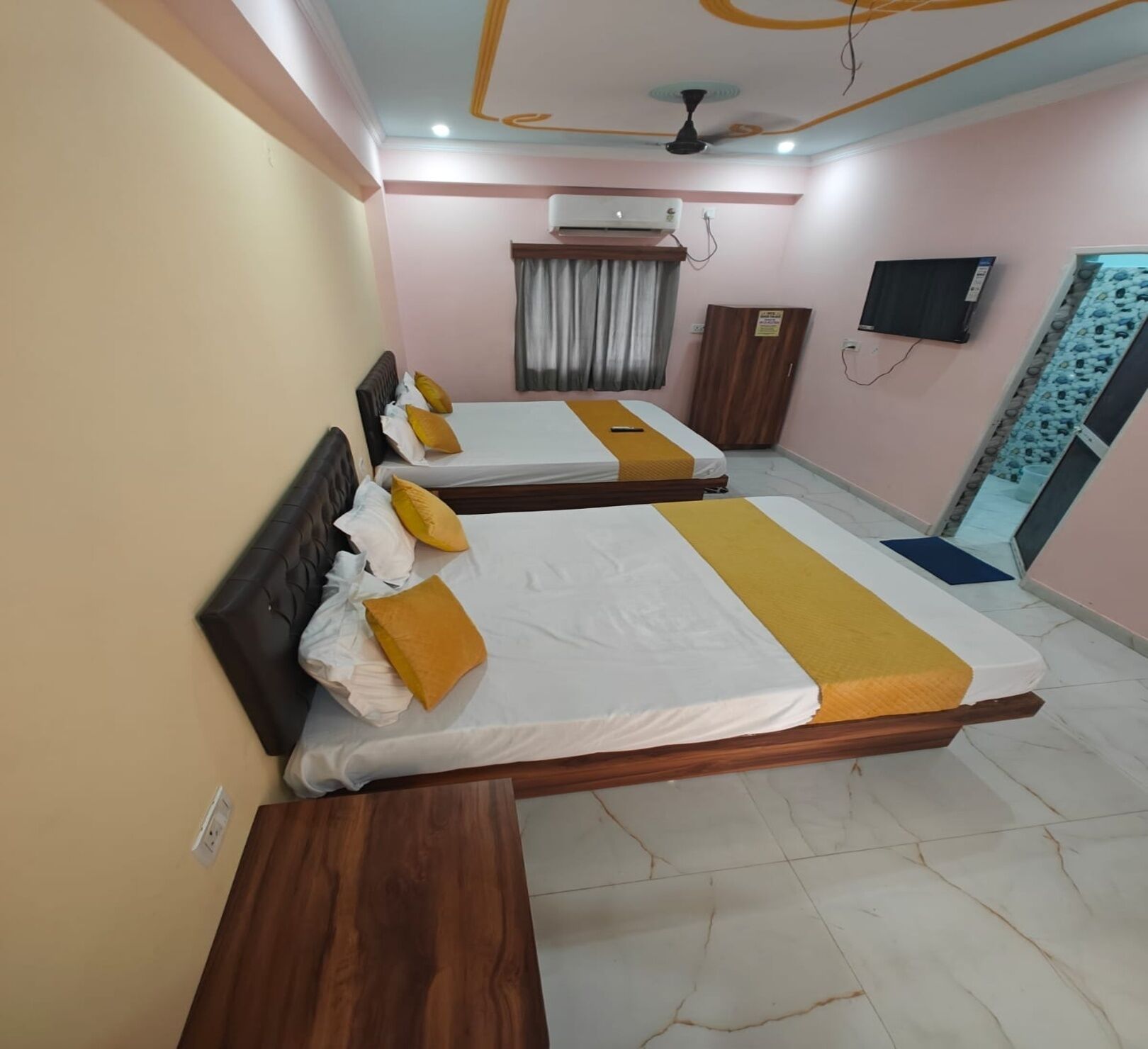 A hotel room with three beds, a ceiling fan, an air conditioning unit, a TV, and a wardrobe.