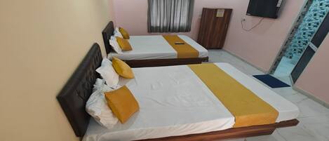 A hotel room with three beds, a ceiling fan, an air conditioning unit, a TV, and a wardrobe.
