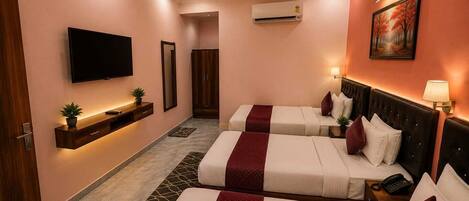 Habitación de hotel con dos camas, televisión, ventilador de techo, aire acondicionado y un cuadro en la pared.