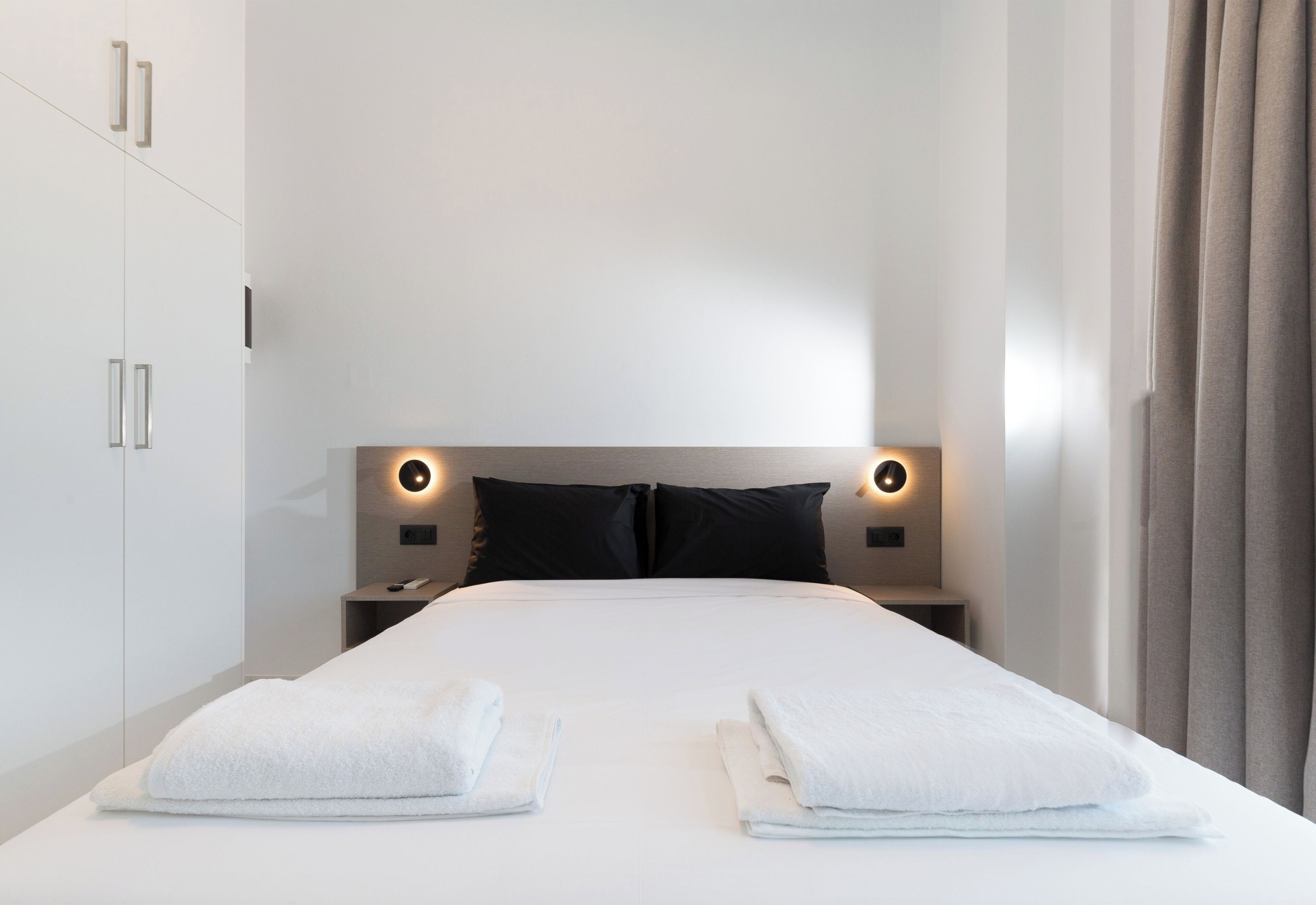 Una habitación de hotel moderna con una cama grande, dos mesitas de noche, un cabecero con iluminación integrada y un armario.