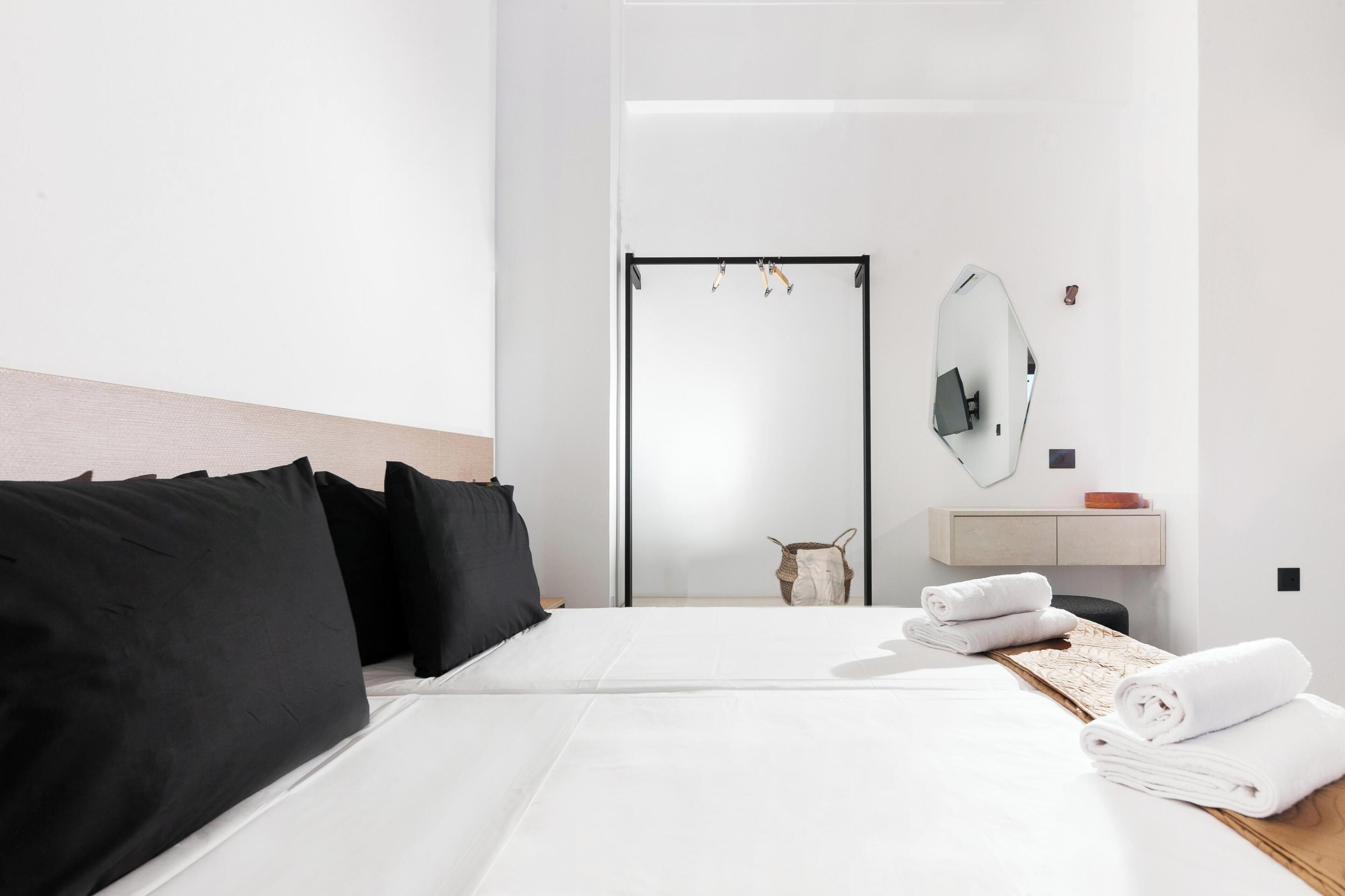 Quarto de hotel com cama, espelho, mesinha com toalhas, cabeceira de madeira e porta para o banheiro.