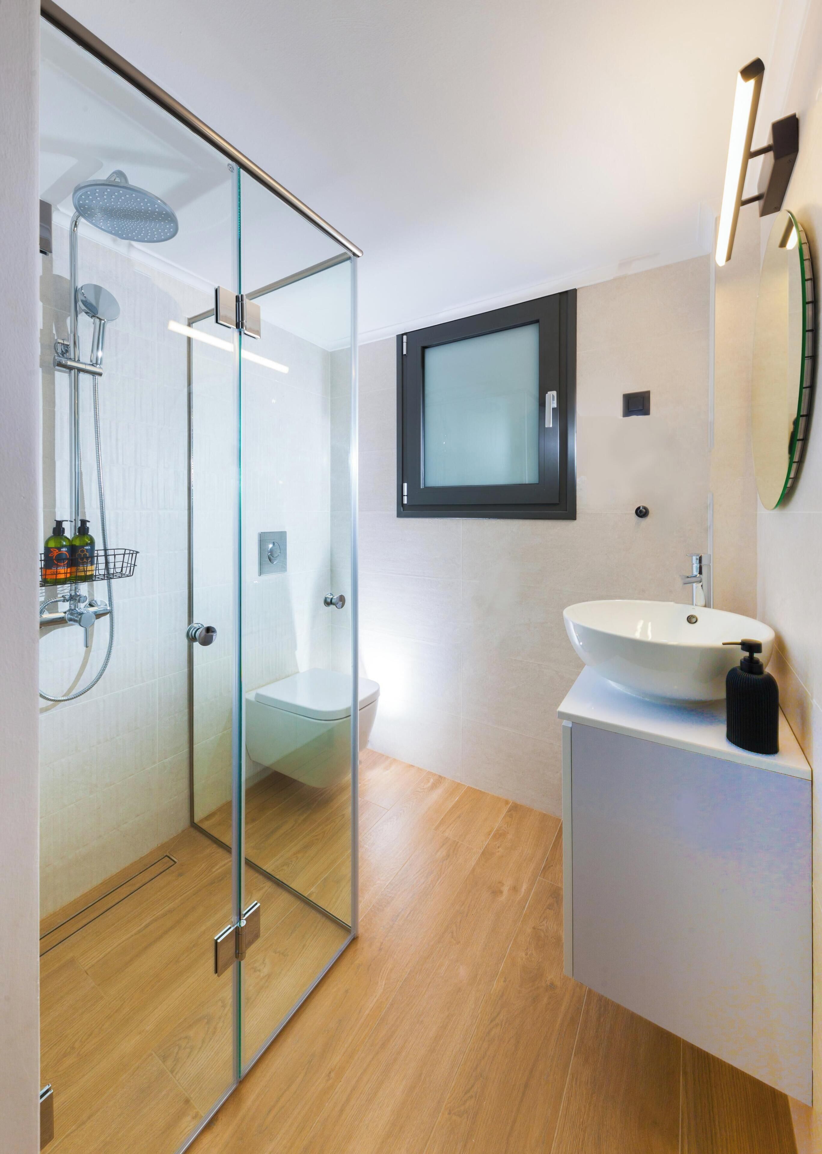 Une salle de bain moderne avec une douche à parois de verre, des toilettes, un lavabo avec un distributeur de savon et un miroir.