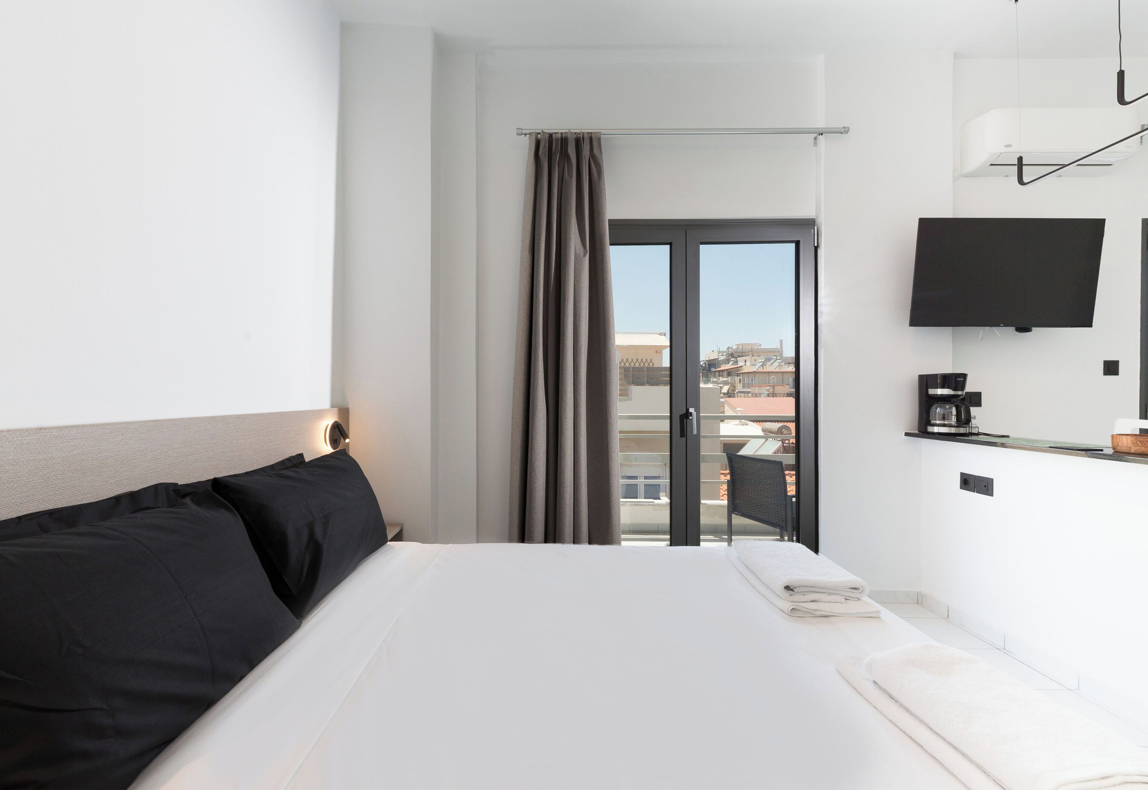 A hotel room with a bed, a TV, a coffee machine, and a view of the city through the window.