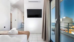 A hotel room with a bed, a TV mounted on the wall, a balcony with a view of the city, and a door leading to another room.