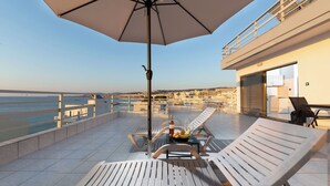 A terrace with two lounge chairs, a table with a bottle and fruit, and an umbrella.