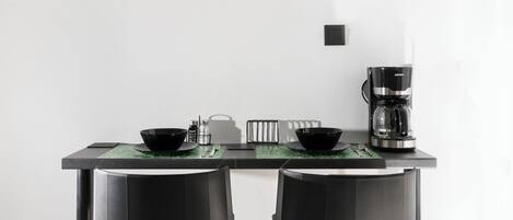 Une cuisine moderne avec deux tabourets de bar noirs, une machine à café et un bol posé sur le comptoir.