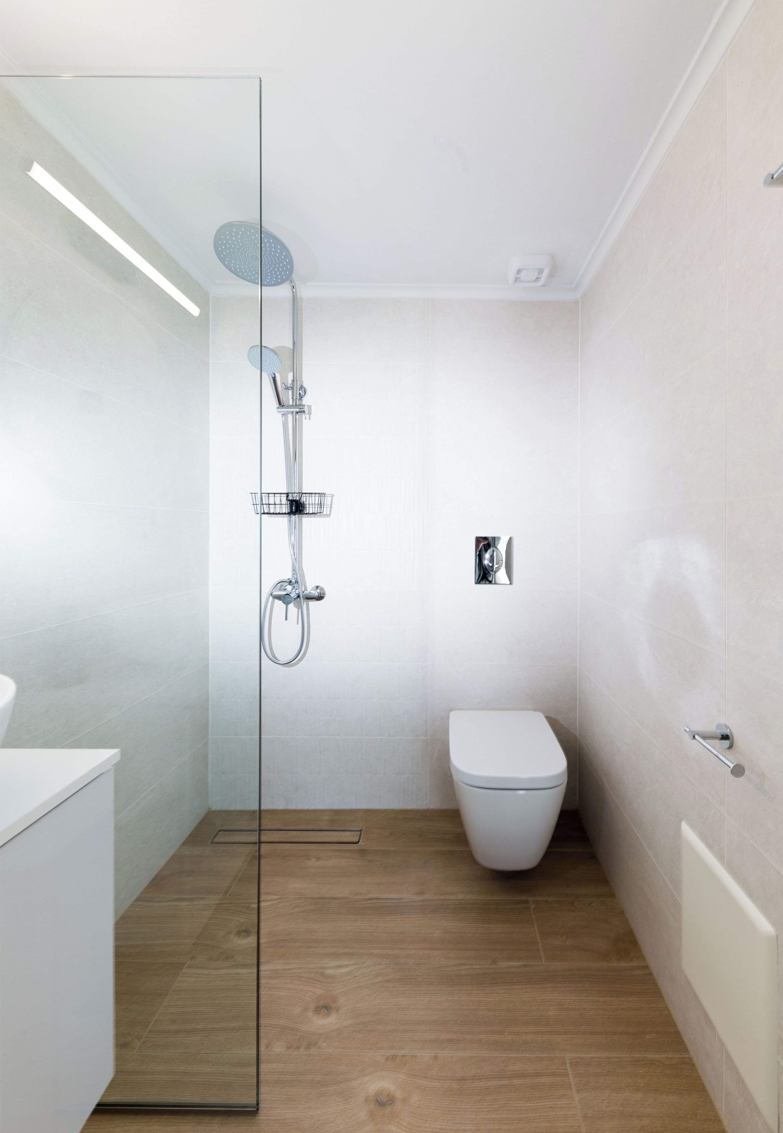 A modern bathroom with a glass shower enclosure, a white toilet, and a wooden floor.