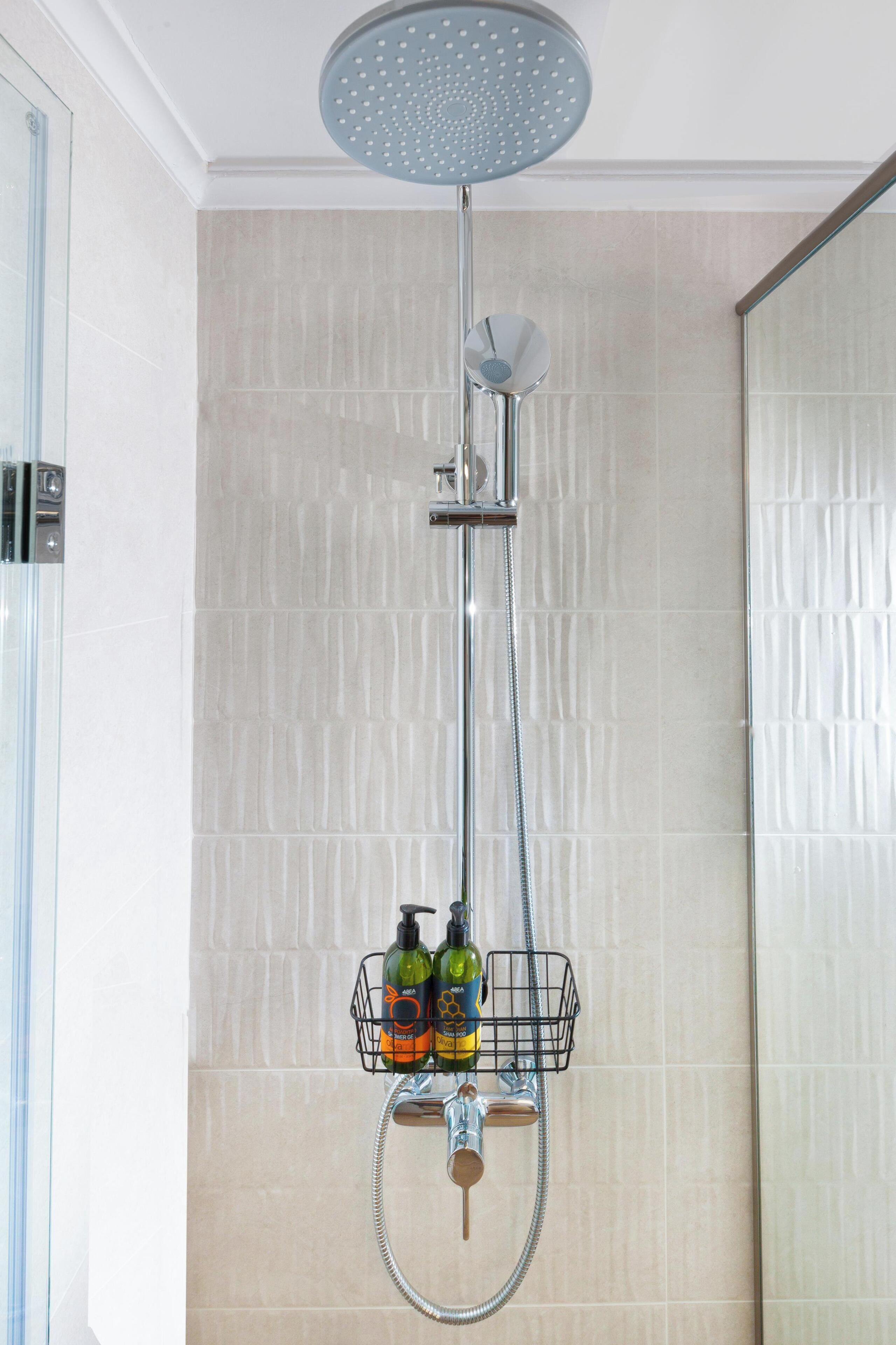 A shower with a rain showerhead, a handheld showerhead, and a wall-mounted faucet. A soap dispenser and a bottle of shampoo are visible.