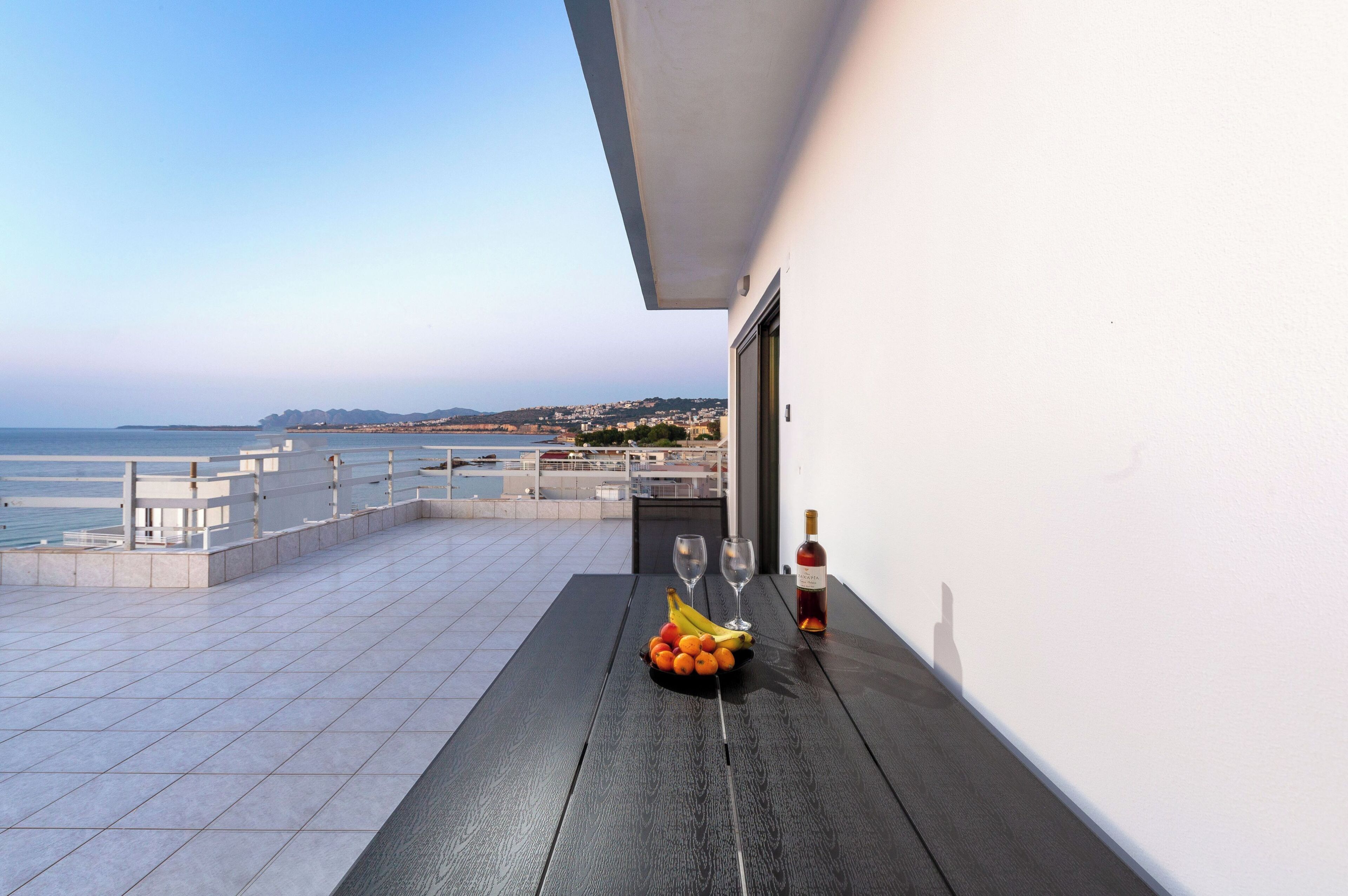 A balcony with a table, a bottle of wine, and a fruit bowl.