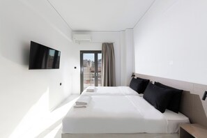 Ein Hotelzimmer mit Bett, Fernseher, Fenster mit Vorhängen und Blick auf Gebäude.