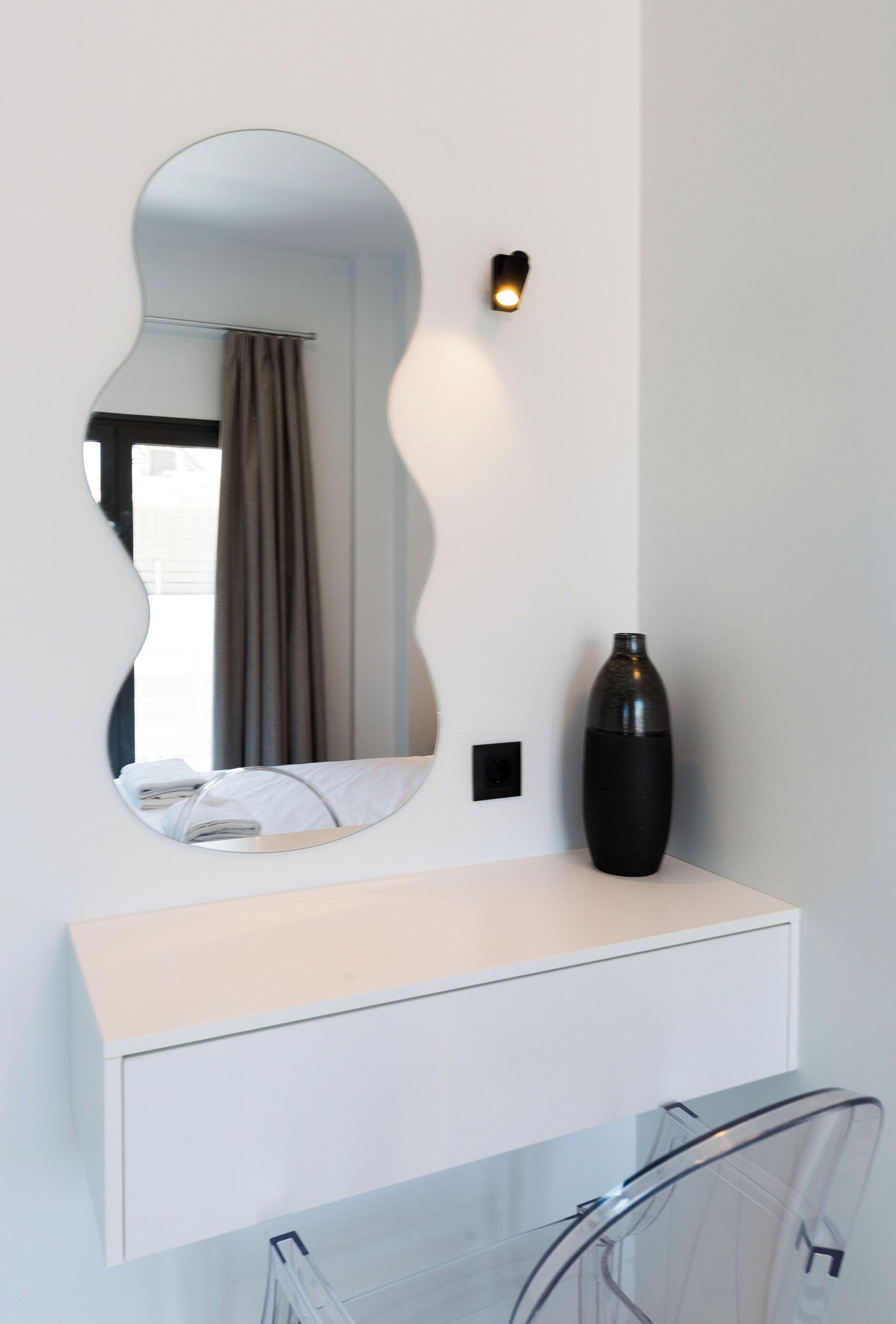 A bathroom with a white vanity, a large mirror, a black vase, and a clear bicycle rack.