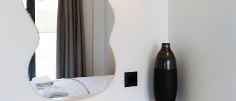 A bathroom with a white vanity, a large mirror, a black vase, and a clear bicycle rack.