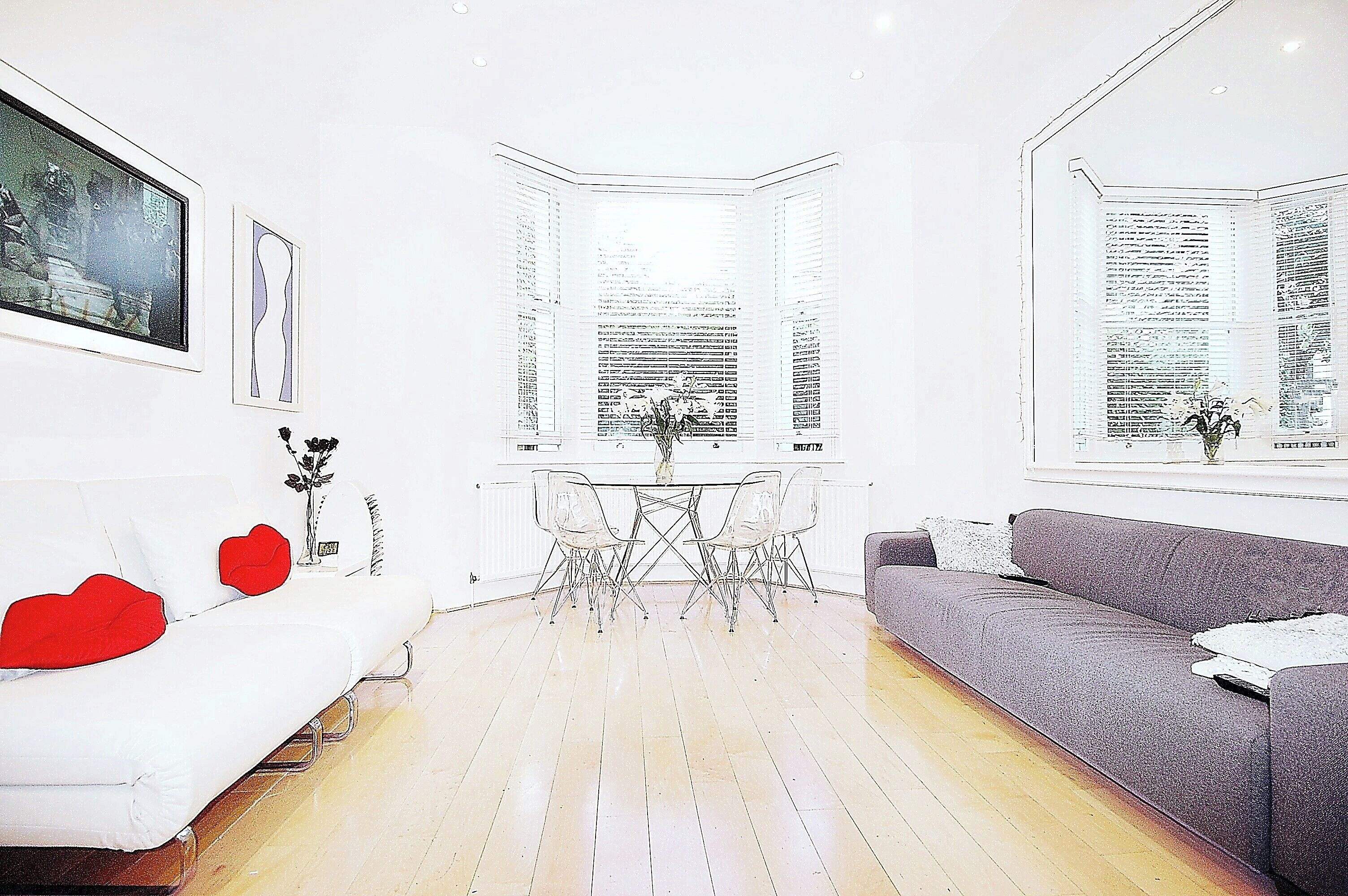 A modern living room with a white sofa, a grey sofa, a dining table with chairs, and large windows.