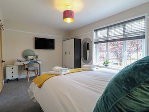 A bedroom with a bed, a desk, a mirror, a wardrobe, and a window with a view.