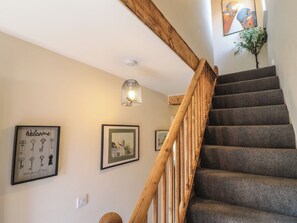 A staircase with wooden railings, a hanging light fixture, and framed artwork on the walls. - The Kingfisher Falls (Melton Mowbray)