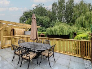 Eine überdachte Terrasse im Freien mit einem runden Tisch und Stühlen, umgeben von einem Holzzaun und üppiger Bepflanzung.