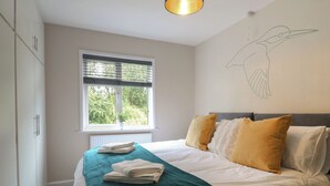 A bedroom with a bed, pillows, a window, a radiator, and a wall with a bird mural. - The Kingfisher Falls (Melton Mowbray)
