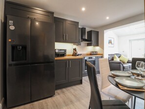 Una cocina moderna con refrigerador, microondas y horno incorporados. Hay un comedor con una mesa dispuesta para dos personas, un sofá y una mesita de centro.