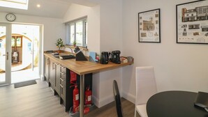 A modern kitchen with a wooden countertop, a sink, and a window. There are two framed pictures on the wall and a clock on the wall. - The Kingfisher Falls (Melton Mowbray)