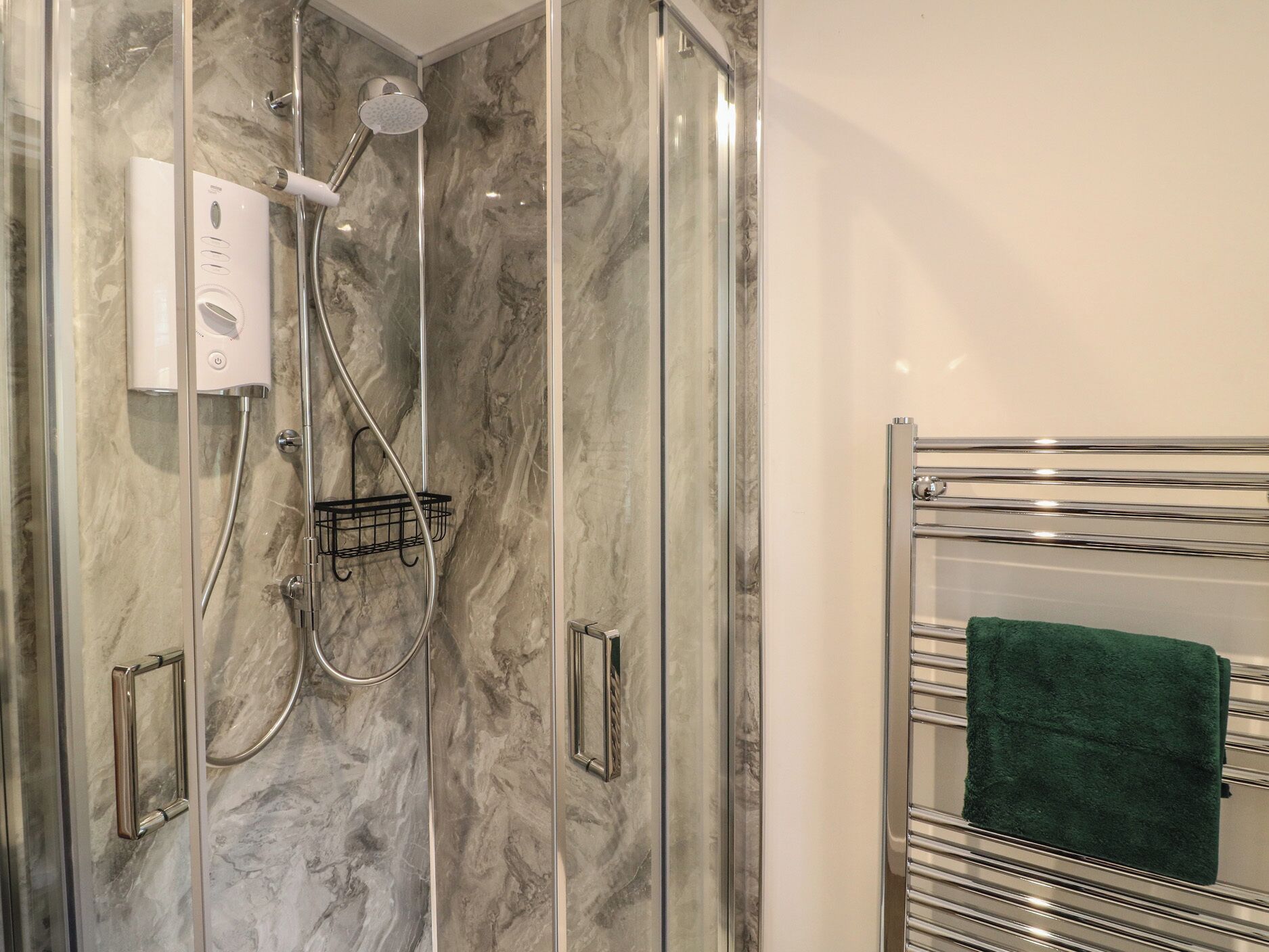 A shower with a handheld showerhead, a wall-mounted control panel, and a towel rack with a green towel.
