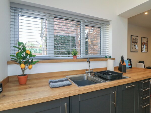A modern kitchen with a wooden countertop, a built-in sink, and a window with blinds. - The Kingfisher Falls (Melton Mowbray)