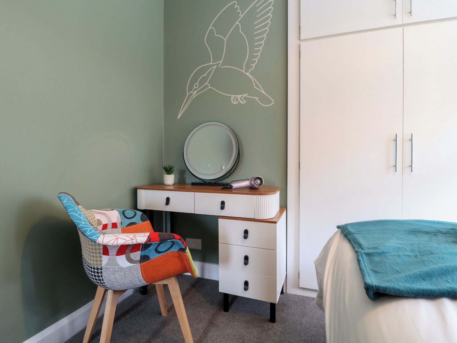 Un dormitorio con cama, una silla, cómoda, espejo y un mural de un pájaro en la pared.