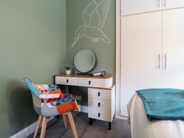 A bedroom with a bed, a chair, a dresser, a mirror, and a wall with a bird mural.