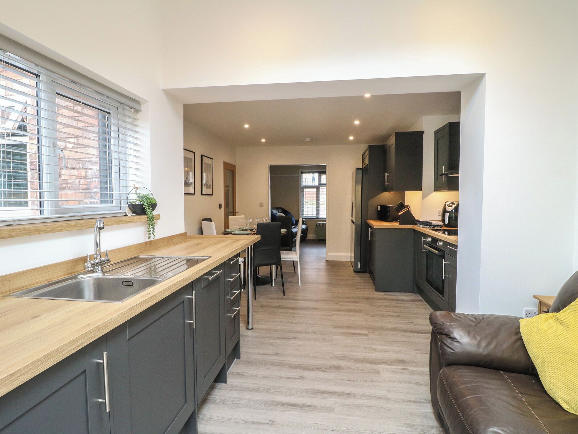 A modern kitchen with a wooden countertop, dark cabinets, and a view into the dining area.