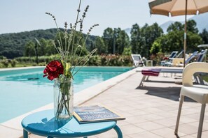 Klar udsigt over en swimmingpool med liggestole og et bord med en bog og blomster.