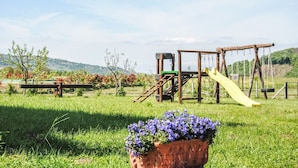 Ein Spielplatz mit Rutsche und Klettergerüsten, umgeben von Gras und Bäumen.
