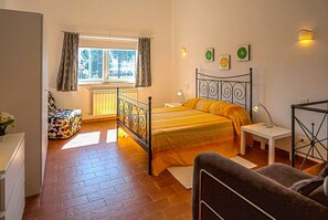 A bedroom with a bed, a bedside table, a chair, a window with curtains, and a radiator. - Houses in Stratola - Apartment 2 (Montella)