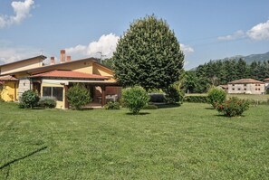 A residential property with a well-maintained lawn, a large tree, and a building with a tiled roof. - Houses in Stratola - Apartment 2 (Montella)