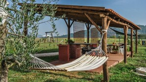 A hammock under a wooden pergola, a brick planter, and a table with chairs in a grassy outdoor setting. - Houses in Stratola - Apartment 2 (Montella)